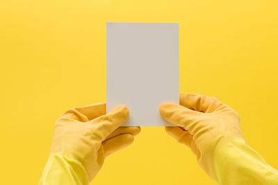 Cropped hand of woman holding paper against yellow background