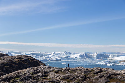 Scenic view of sea by snowcapped mountains against sky