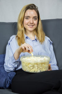 Portrait of young woman having popcorn while sitting on sofa at home