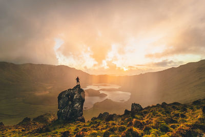 Man standing on rock against sky during sunset