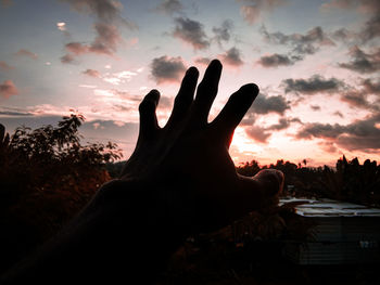 Silhouette person hand against sky during sunset