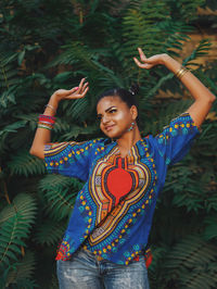 Portrait of young woman with arms outstretched standing against trees