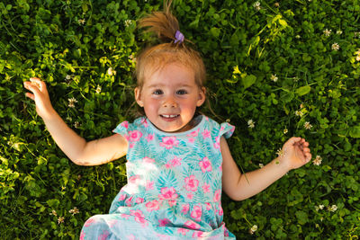 Young girl lying on grass laughing and looking up. 2-3 years old child in nature on sunny summer day