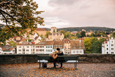 Rear view of couple sitting on bench against buildings