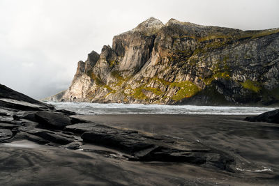 Scenic view of sea by mountain against sky