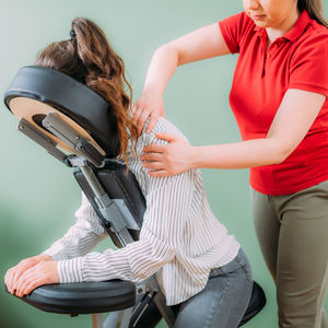 Female employee sitting on a portable massage chair in business office. therapist massaging 