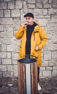 Man smoking cigarette while standing by garbage bin against wall