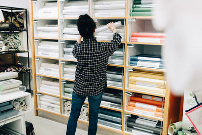 Rear view of senior saleswoman arranging wallpapers in rack