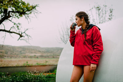 Young woman looking away having drink standing by built structure