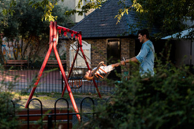 Man pushing while girl sitting on swing in playground