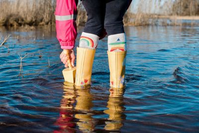 Child's feet in rain boots in the water with a spade playing