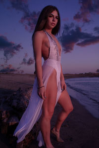 Young woman standing on beach against sky during sunset