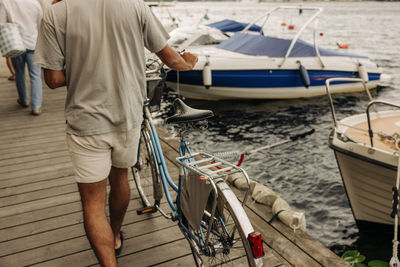 Rear view of man wheeling bicycle on pier at harbor