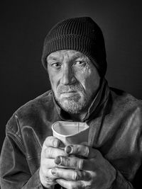 Poor, homeless man begging with paper cup in his hand.