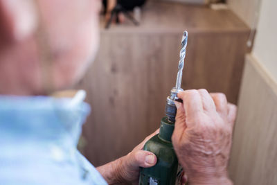 Crop unrecognizable aged male preparing power screwdriver with nozzle while working in light house room