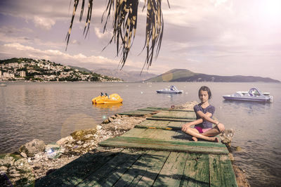 Young woman sitting in sea against sky