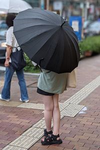 Low section of woman with umbrella walking on footpath