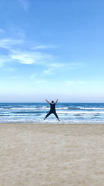 Rear view of man jumping at beach against blue sky