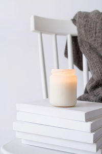 Candle mockup design. cozy interior with white chair, warm plaid, books and autumn leaves