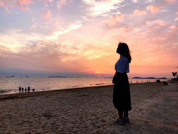 Full length of woman standing at beach against sky during sunset