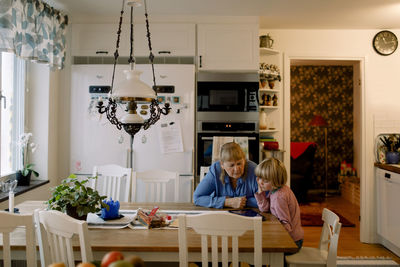 Grandmother and grandson using digital tablet while sitting at dining table