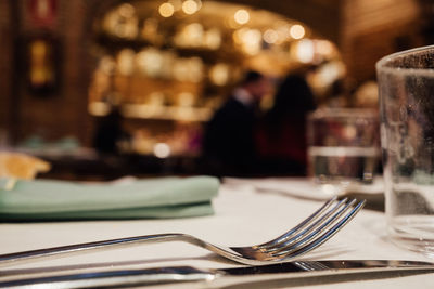 Glasses, fork, knife served for dinner in restaurant with cozy interior.blurred people enjoying food