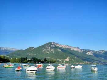 Boats on lake by mountain against clear blue sky