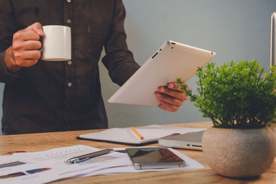 Midsection of man holding coffee cup on table