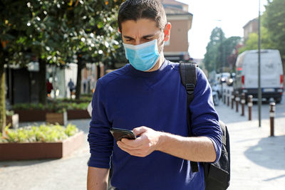 Man wearing mask using mobile phone while standing on street