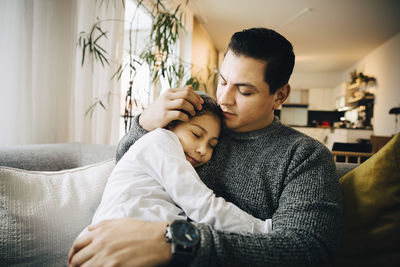 Girl sleeping while hugging father on sofa at home