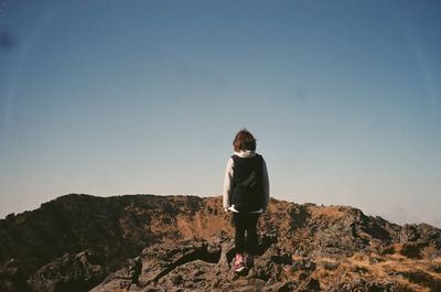 Rear view of young woman standing on mountain against clear sky