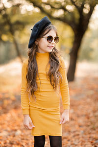 Funny cute kid girl 4-5 year old wear sun glasses and yellow knitted dress posing over nature autumn