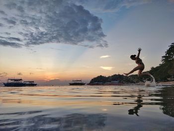 People in mid-air by water against sky during sunset