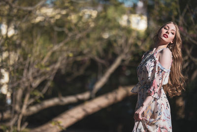 Beautiful young woman standing against trees in park