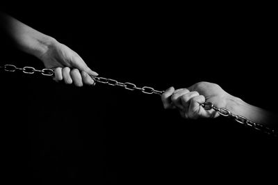 Cropped hand of people pulling chain against black background