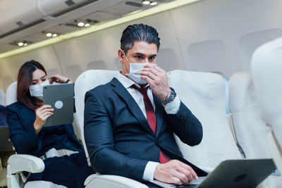 Businessman using laptop in plane during pandemic