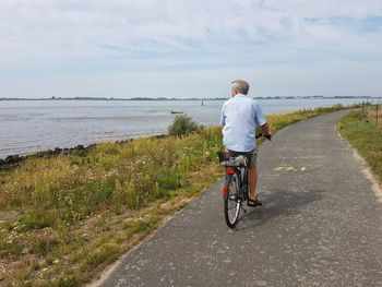 Rear view of man riding bicycle on road with sea in background against sky