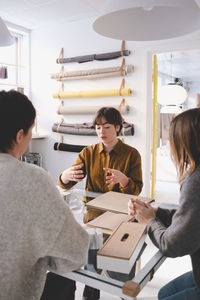 Young female design professional discussing with colleagues at desk in workshop