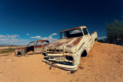 Abandoned car on field against blue sky