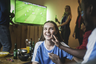 Man applying face paint on woman cheek while watching soccer match at home