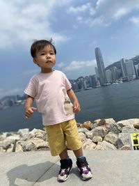 Side view of asian cute boy standing at harbour against sky