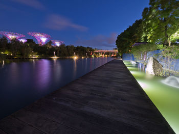 Illuminated river amidst trees against sky at night