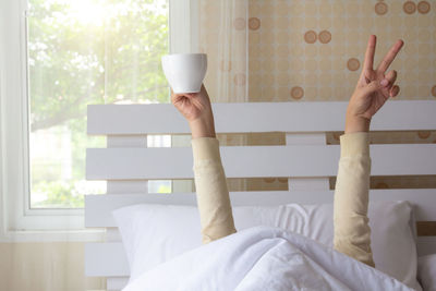 Woman holding coffee cup on bed at home