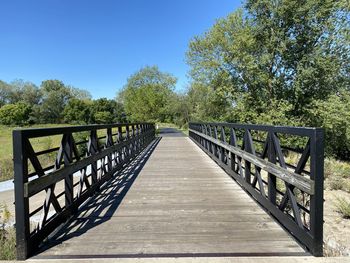 Footbridge amidst trees against clear blue sky