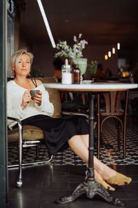 Blond stylish woman sitting at table in cafe with cup of coffee