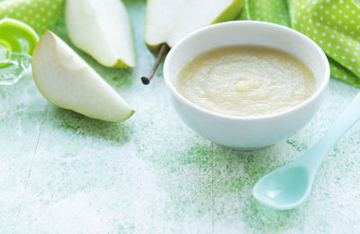 Bowl with baby food and pears on table