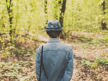 Rear view of woman wearing denim shirt and hat while standing in forest