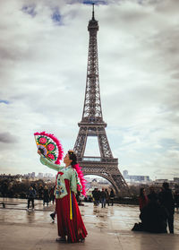 Woman in traditional clothing with hand fan standing against eiffel tower