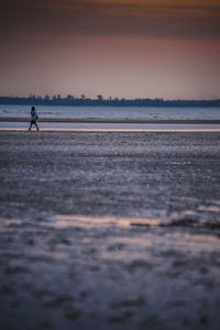 Woman walking at beach against sky during sunset