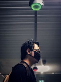 Low angle view of young man against illuminated ceiling and lights.